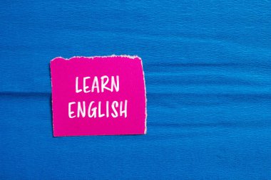 Yırtık pembe kağıt parçasına mavi arkaplanlı İngilizce mesaj yazmayı öğren. Kavramsal İngilizce öğrenme sembolü. Boşluğu kopyala.