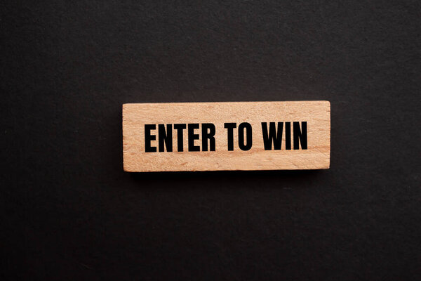 Enter to win message written on single wooden block with black background. Conceptual enter to win symbol. Copy space.
