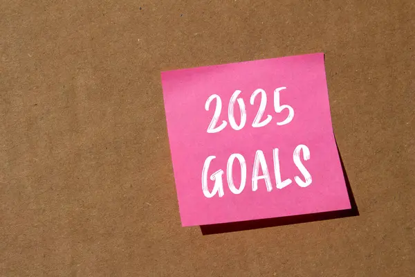 Stock image 2025 goals message written on pink paper with cardboard background. Conceptual 2025 goals symbol. Copy space.