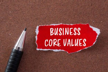 Business core values message written on ripped torn red paper and a pen with brown background. Conceptual business core values symbol. Copy space. clipart