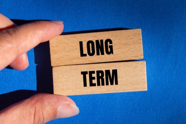 Mavi arka plandaki tahta bloklara yazılmış uzun vadeli bir mesaj. Kavramsal uzun dönem sembolü. Boşluğu kopyala.