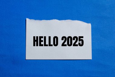 Merhaba 2025. Yırtık beyaz kağıt parçasına mavi arkaplan ile yazılmış mesaj. Kavramsal merhaba 2025 sembolü. Boşluğu kopyala.