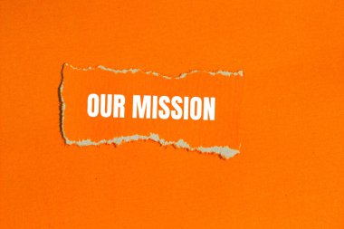 Görev mesajımız turuncu arka planlı yırtık turuncu kağıda yazılmış. Görevimizin sembolü kavramsal. Boşluğu kopyala.