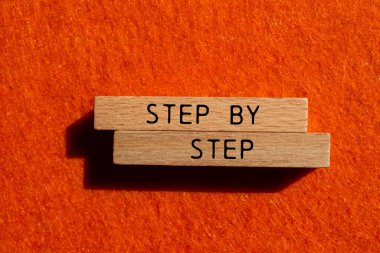 Tahta bloklara, turuncu keçeli arka planda adım adım yazılmış mesaj. Kavramsal adım adım sembolü. Boşluğu kopyala.