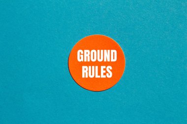 Ground rules message written on round orange sticker with blue background. Conceptual ground rules symbol. Copy space. clipart