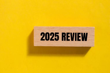 2025 gözden geçirme mesajı ahşap blokta, sarı arka planda yazılmış. Kavramsal 2025 değerlendirme sembolü. Boşluğu kopyala.