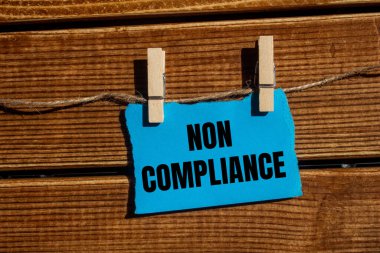 Non compliance message written on ripped blue torn paper piece with wooden background. Conceptual non compliance symbol. Copy space. clipart