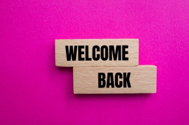 Welcome back message written on wooden blocks with pink background. Conceptual welcome back symbol. Copy space. clipart