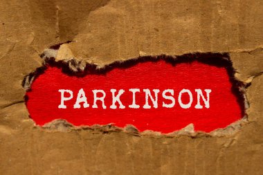Kırmızı arka planda yırtık karton kağıda Parkinson mesajı yazılmış. Kavramsal Parkinson sembolü. Boşluğu kopyala.