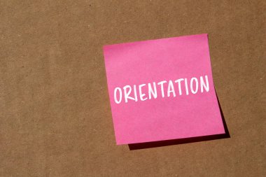 Kahverengi arka planda pembe kağıda oryantasyon mesajı yazılmış. Kavramsal yönelim sembolü. Boşluğu kopyala.