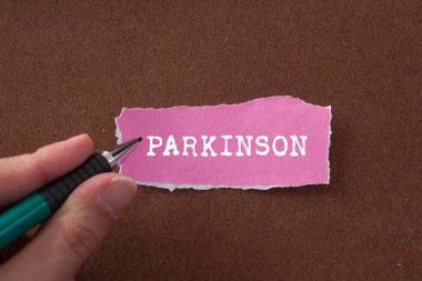 Parkinson mesajı kahverengi arka plandaki yırtık pembe kağıda yazılmış. Kavramsal Parkinson sembolü. Boşluğu kopyala.