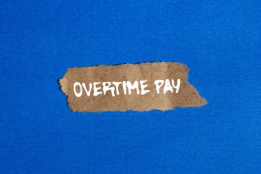 Fazla mesai ödemesi mesajı mavi arka plandaki yırtık kahverengi kağıt parçasına yazılmış. Kavramsal fazla mesai ödeme sembolü. Boşluğu kopyala.