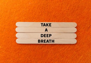 Turuncu arka planda tahta çubuklara yazılmış derin bir nefes mesajı alın. Kavramsal bir nefes alma sembolü. Boşluğu kopyala.