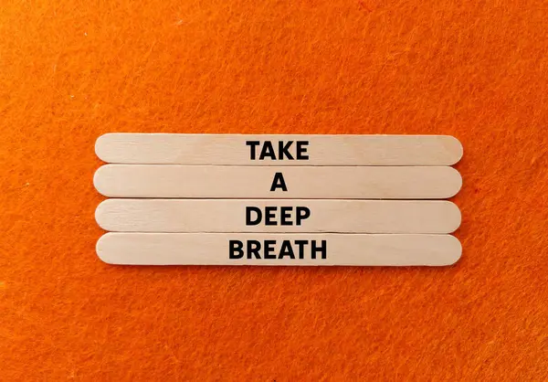 Turuncu arka planda tahta çubuklara yazılmış derin bir nefes mesajı alın. Kavramsal bir nefes alma sembolü. Boşluğu kopyala.