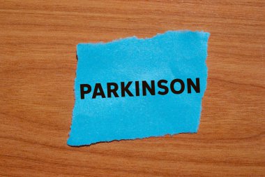 Parkinson mesajı ahşap arka planda yırtık mavi kağıt parçasına yazılmış. Kavramsal Parkinson sembolü. Boşluğu kopyala.