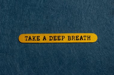 Gri arka planda sarı tahta çubuğa yazılmış derin bir nefes mesajı alın. Kavramsal bir nefes alma sembolü. Boşluğu kopyala.