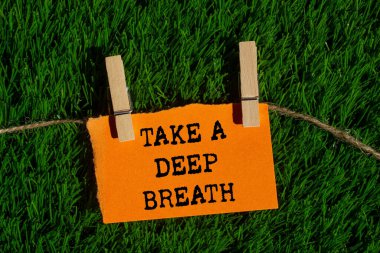 Yırtık turuncu kağıt parçasına yeşil çimen arka planına yazılmış derin bir nefes mesajı alın. Kavramsal bir nefes alma sembolü. Boşluğu kopyala.