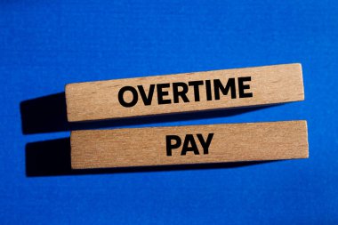 Fazla mesai ödemesi mesajı mavi arka plandaki tahta bloklara yazılmış. Kavramsal fazla mesai ödeme sembolü. Boşluğu kopyala.