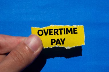 Fazla mesai ödemesi mesajı mavi arka planda yırtık sarı kağıt parçasına yazılmış. Kavramsal fazla mesai ödeme sembolü. Boşluğu kopyala.