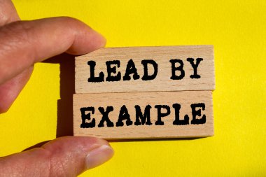 Sarı arkaplandaki tahta bloklara yazılmış örnek mesajla öncülük edin. Örnek sembolle kavramsal liderlik. Boşluğu kopyala.