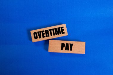 Fazla mesai ödemesi mesajı mavi arka plandaki tahta bloklara yazılmış. Kavramsal fazla mesai ödeme sembolü. Boşluğu kopyala.