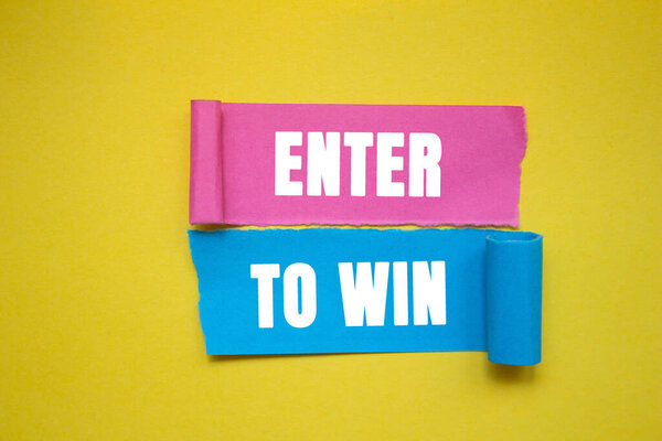Enter to win message written on ripped torn color paper pieces on yellow background. Conceptual enter to win symbol. copy space.