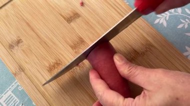 Person cutting Turkish sucuk sausage with knife on wooden board