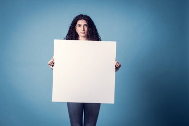 Güzel kıvırcık kadın mavi arka planda boş ilan panosu tutuyor.