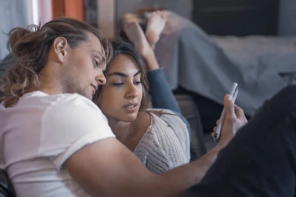 stock image Cheerful couple of romantic serious caucasian guys sharing a night message in living room searching and messaging watching their cellphone device. Male fun guy enjoyng his life looking a smart girl