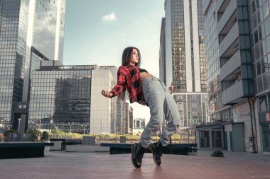 Kırmızı tişört, kot pantolon ve siyah botlarla ayak parmaklarında poz veren şık beyaz hip hop dansçısının fotoğrafı ve arka planda şehir merkezi olan bir üstten. Hareket halindeki modelin arkadan çekimleri