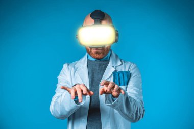 Mavi arka planı ve beyaz önlüklü, 3D gözlüklü bir erkek doktorun fotoğrafı.