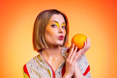 Güzel, sarışın, açık mavi gözlü, turuncu gözlü, parlak sarı arkaplanlı öpücükler yollayan bir kadın.