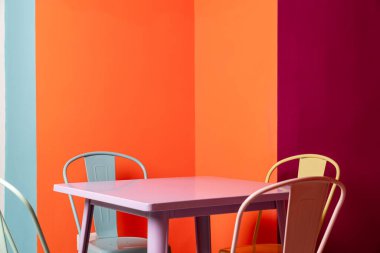 Sarı, mavi renkli sandalyeleri ve turuncu, sarı, mor ve mavi arka planı olan pembe fast food masası.