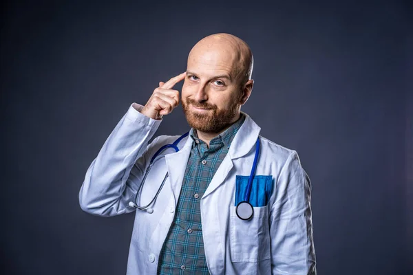 青い背景と医療白いコートで考えるひげとステスコープを持つ医師の写真 ロイヤリティフリーのストック写真