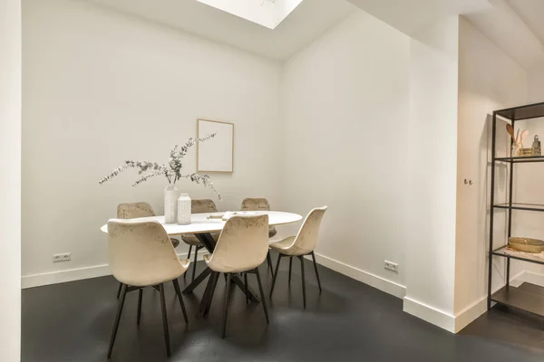 Modern minimalist style interior design of studio apartment with open white kitchen and dining zone with table and chairs illuminated by loft style lamp