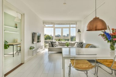 Çağdaş dairenin geniş odasındaki dinlenme odası ve mutfağın yakınındaki sandalyeli ve çiçekli masa.