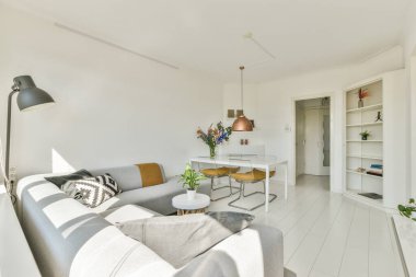 Çağdaş dairenin geniş odasındaki dinlenme odası ve mutfağın yakınındaki sandalyeli ve çiçekli masa.