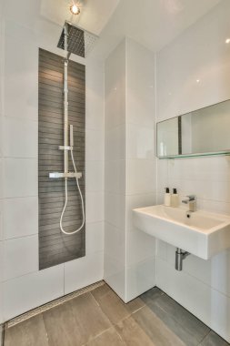 Çağdaş dairenin küçük fayanslı banyosunda lavabo ve duş arasında bulunan sifon tuvaleti