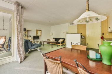 Çağdaş dairenin geniş odasındaki dinlenme odası ve mutfağın yakınındaki sandalyeli ve çiçekli masa.