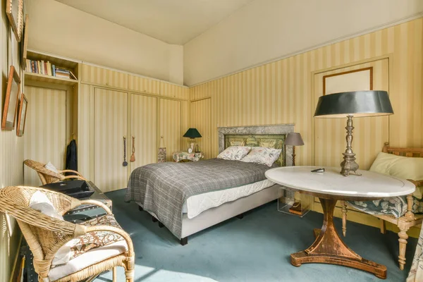 stock image Stylish lamp glowing on vintage bedside table with books and magazines near bed