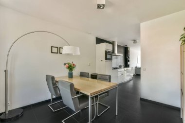 Çağdaş dairenin geniş odasındaki dinlenme odası ve mutfağın yakınındaki sandalyeli ve çiçekli masa.