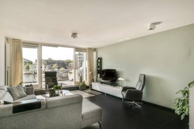 Çağdaş dairenin geniş odasındaki dinlenme odası ve mutfağın yakınındaki sandalyeli ve çiçekli masa.