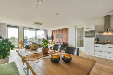 Çağdaş dairenin geniş odasındaki dinlenme odası ve mutfağın yakınındaki sandalyeli ve çiçekli masa.