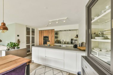 Çağdaş dairenin geniş odasındaki dinlenme odası ve mutfağın yakınındaki sandalyeli ve çiçekli masa.