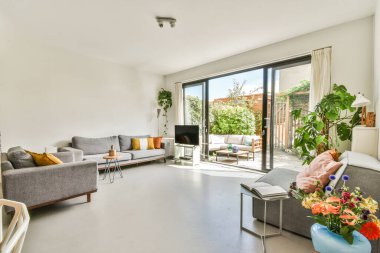 Çağdaş dairenin geniş odasındaki dinlenme odası ve mutfağın yakınındaki sandalyeli ve çiçekli masa.