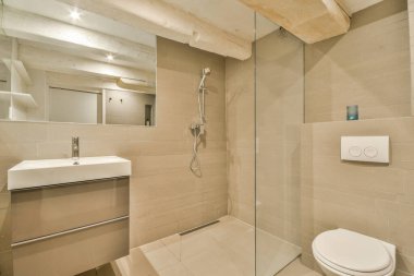 Evdeki modern tuvalette asılı duran banyo musluğu ile duvar arasındaki cam bölme.