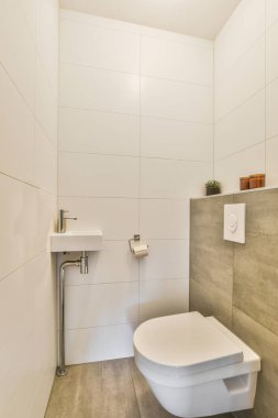 Duvar asılmış tuvalet ve küçük lavabo beyaz ve bej fayanslı tuvalet odasında.