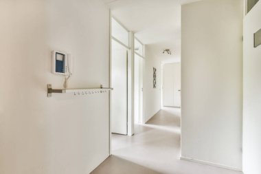 Beyaz duvarları ve kapıları olan dar koridor modern apartmanda pencereleri olan geniş odaya açılıyor.
