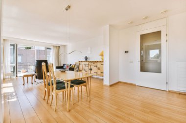 Günümüz minimalist tasarımı. Hafif stüdyo dairesinin ahşap masası ve oturma odası ile beyaz duvarları ve parke zemini arasında yemek masası ve sandalyeleri var.