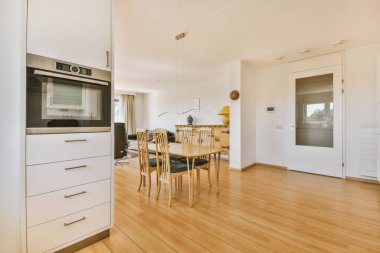 Günümüz minimalist tasarımı. Hafif stüdyo dairesinin ahşap masası ve oturma odası ile beyaz duvarları ve parke zemini arasında yemek masası ve sandalyeleri var.